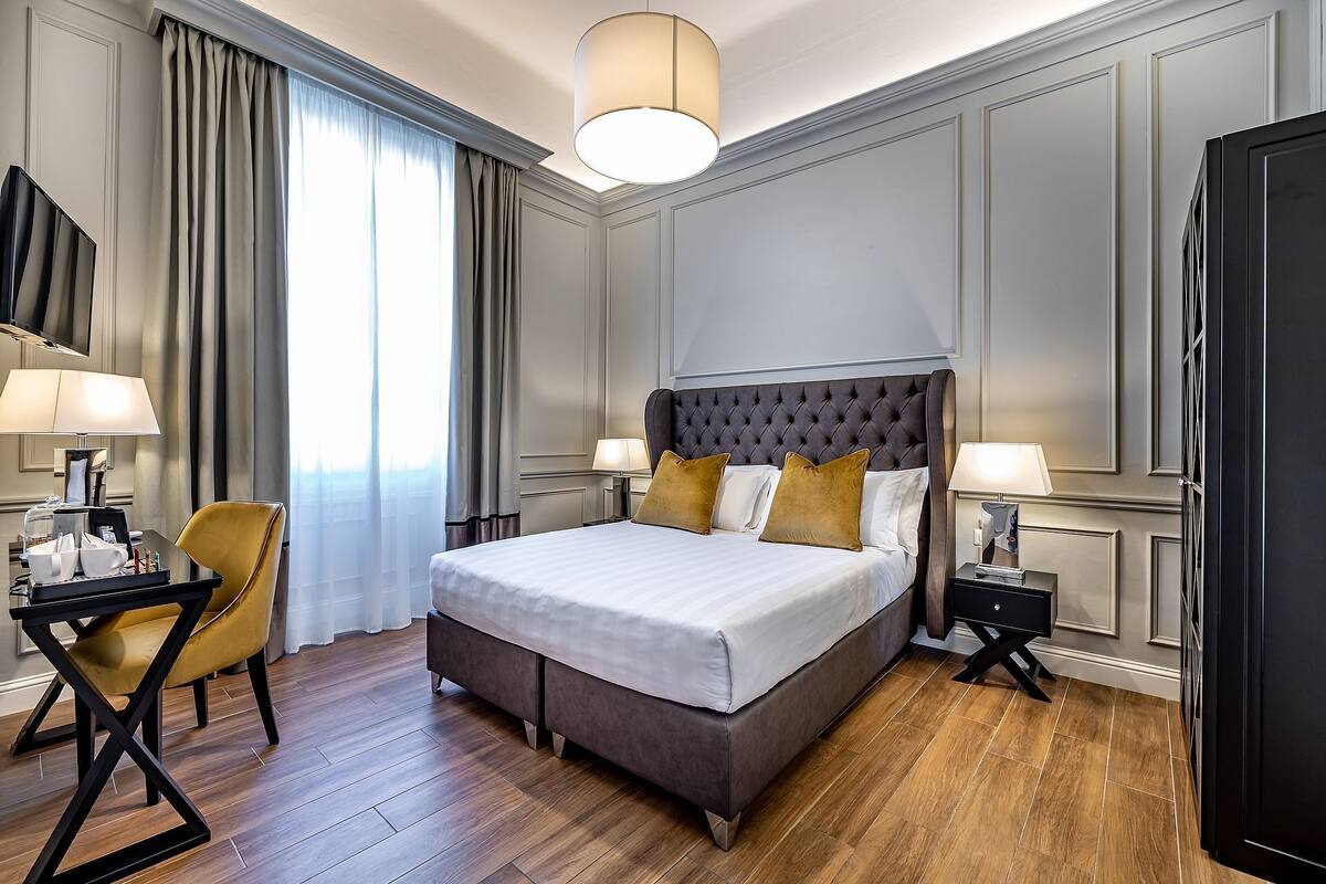 A hotel room with a large bed, two bedside tables with lamps, a chair, and a desk with a tray of toiletries.