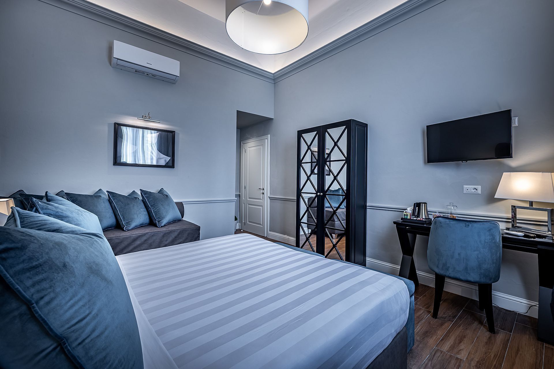 A hotel room with a bed, a desk, a chair, a TV, and a wardrobe.