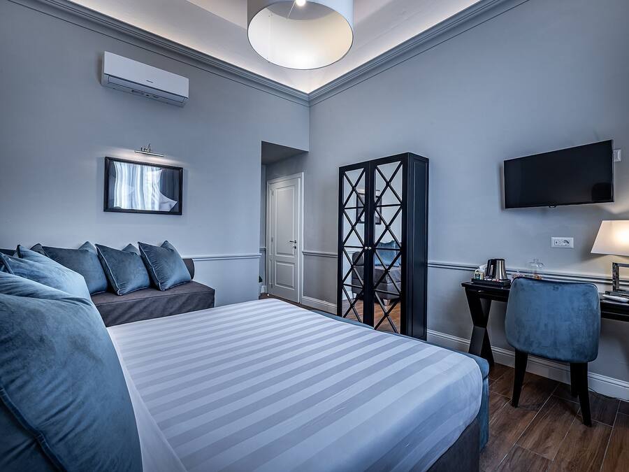 A hotel room with a bed, a desk, a chair, a TV, and a wardrobe.