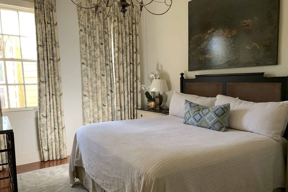 Quarto com uma cama grande, mesa de cabeceira com abajur, quadro na parede e cortinas.