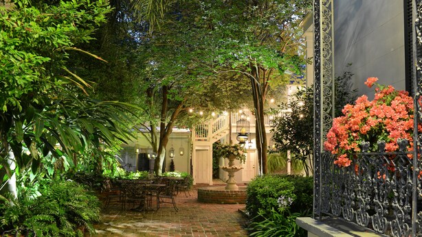 A brick-paved courtyard with a dining area, surrounded by lush greenery and a decorative iron fence. - Terrell House Bed & Breakfast (New Orleans)