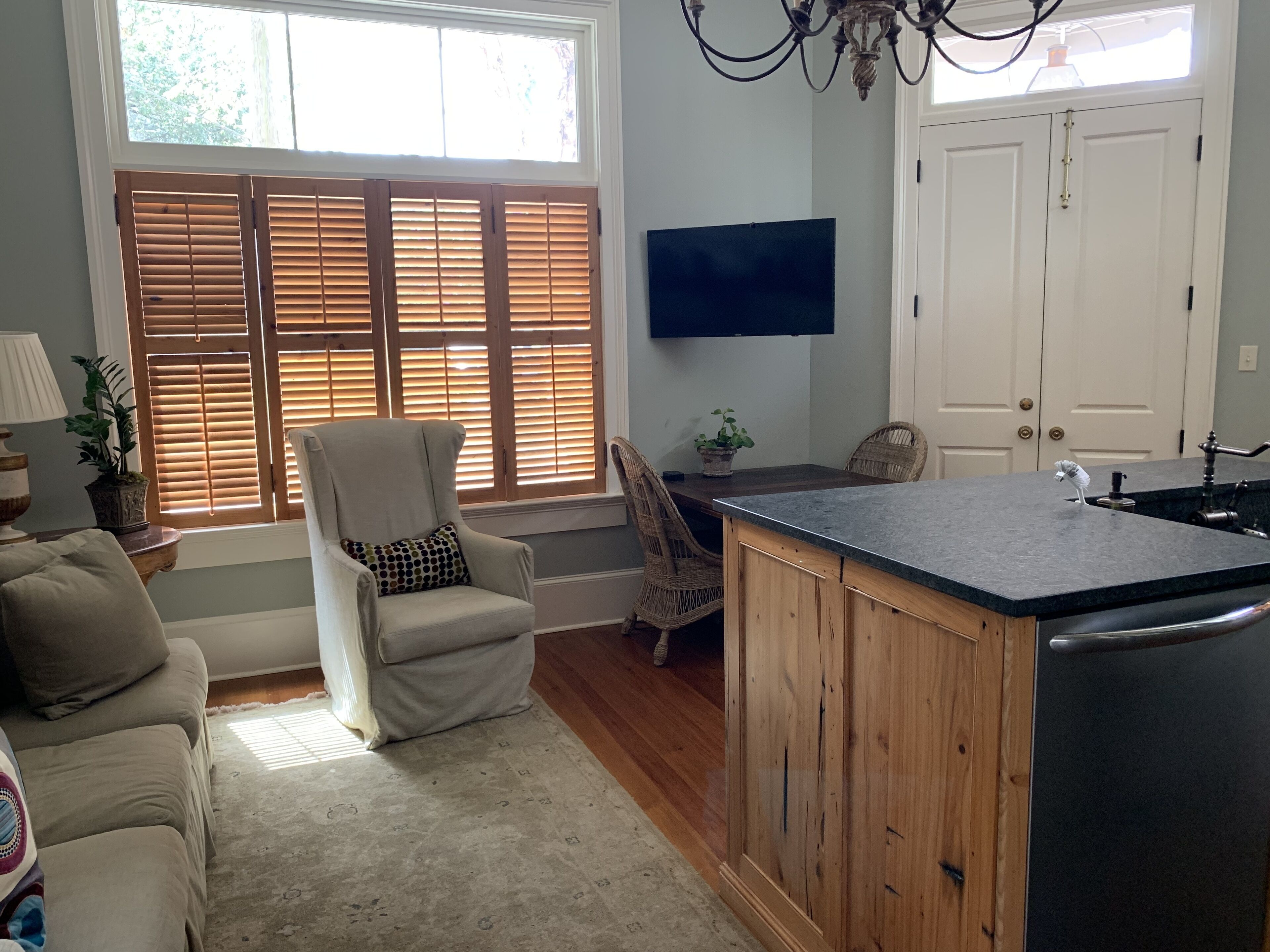 A kitchen with a wooden island, a dining area with wicker chairs, and a large window with blinds.