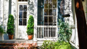 A white building with a brick staircase, potted plants, and a hanging birdcage. - Terrell House Bed & Breakfast (New Orleans)
