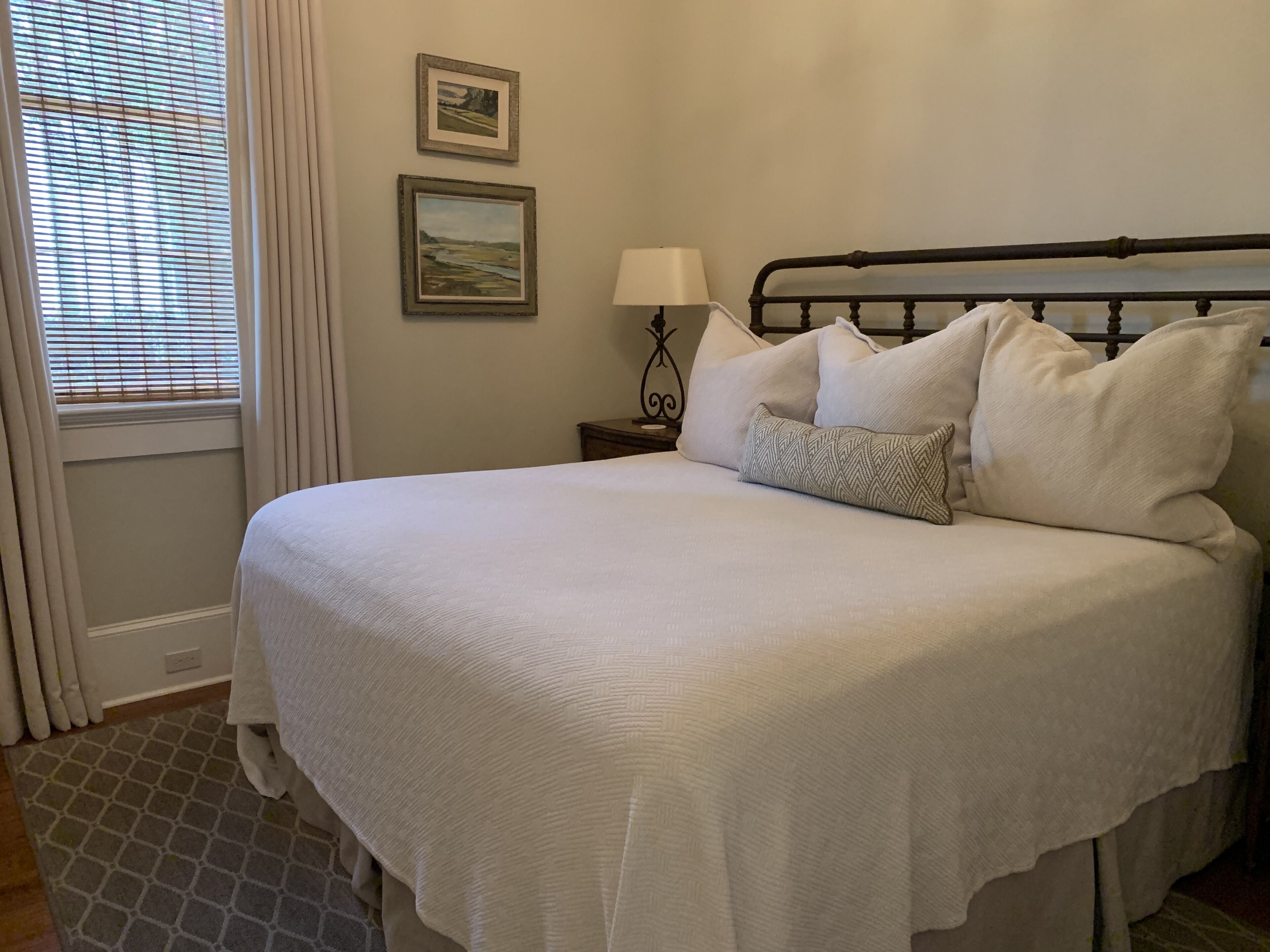 A neatly made bed with a white comforter and pillows, a bedside table with a lamp, and two framed pictures on the wall.