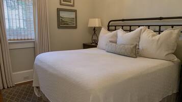 A neatly made bed with a white comforter and pillows, a bedside table with a lamp, and two framed pictures on the wall.