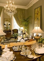 A dining area with a chandelier, green curtains, and a table set for a meal.