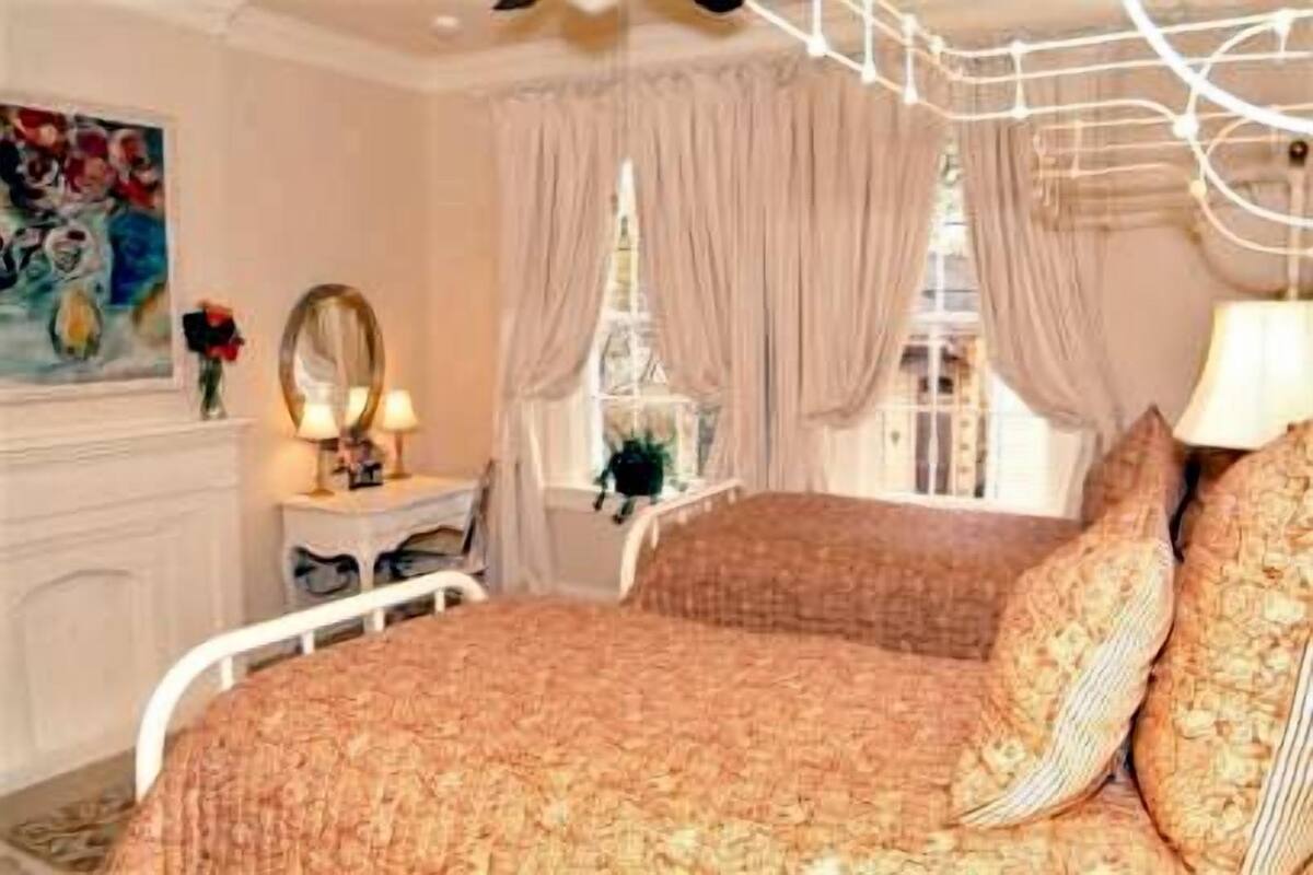 Quarto com cama, penteadeira, espelho e janela com cortinas.
