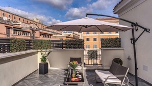 A rooftop terrace with a table set for two, a sofa, and a large umbrella. - Hotel Zara (Rome)