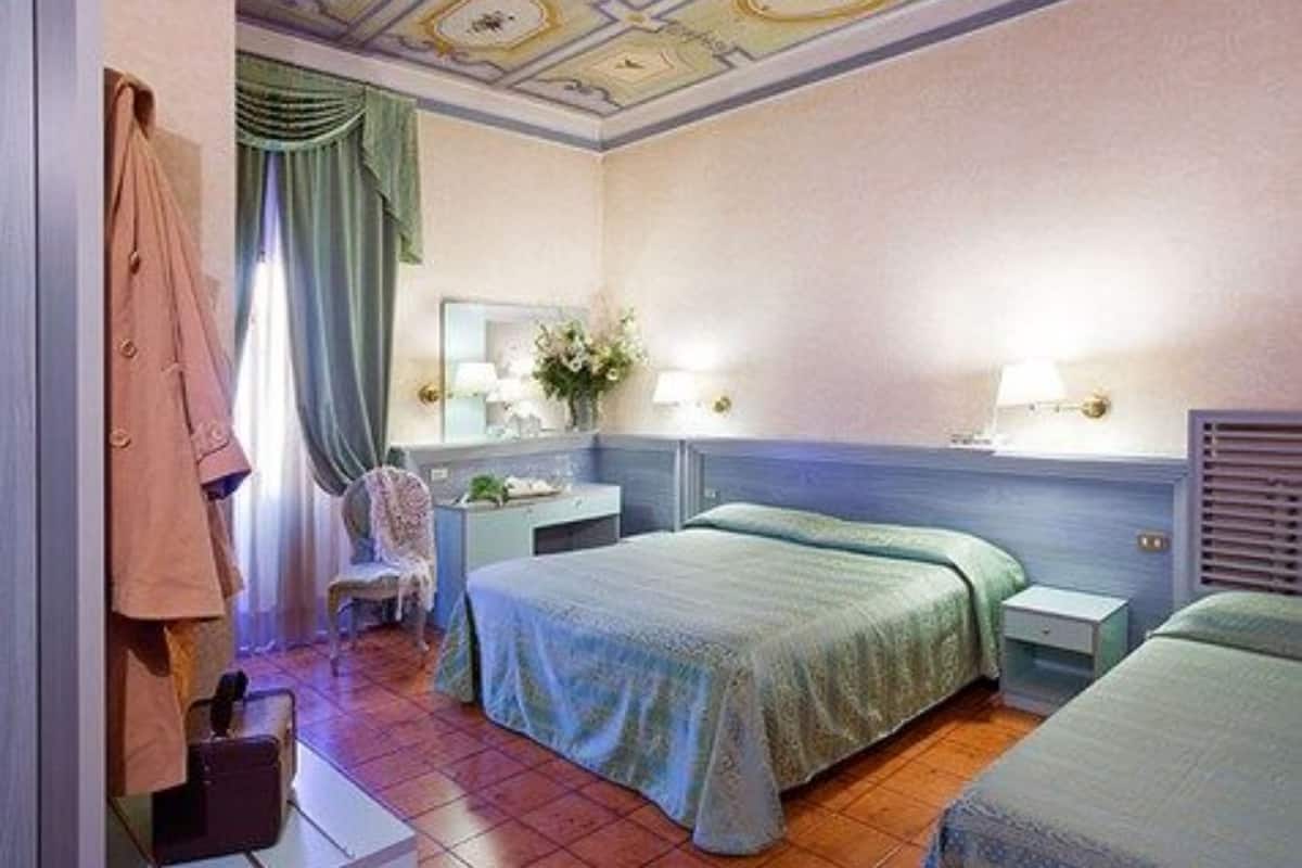 A hotel room with two beds, a desk, a chair, a wardrobe, and a bathroom.