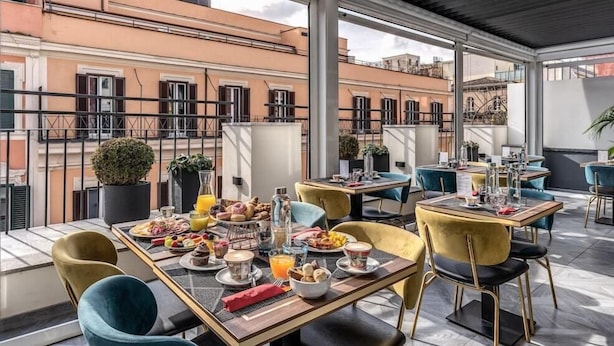 A rooftop dining area with tables set for breakfast, outdoor seating, and a view of the cityscape. - Hotel Zara (Rome)