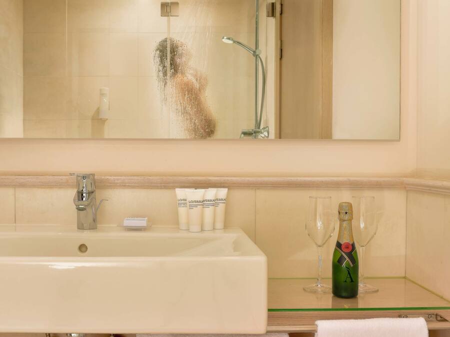 A bathroom with a large mirror, a sink, a shower, and a bottle of champagne on the counter.