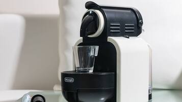 Uma máquina de café Delonghi com um suporte de vidro para chávenas numa superfície refletora.