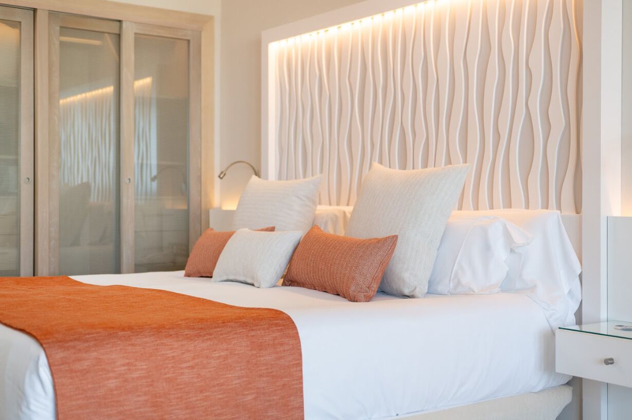 Un dormitorio moderno con cama, ropa de cama blanca y un original cabecero ondulado.