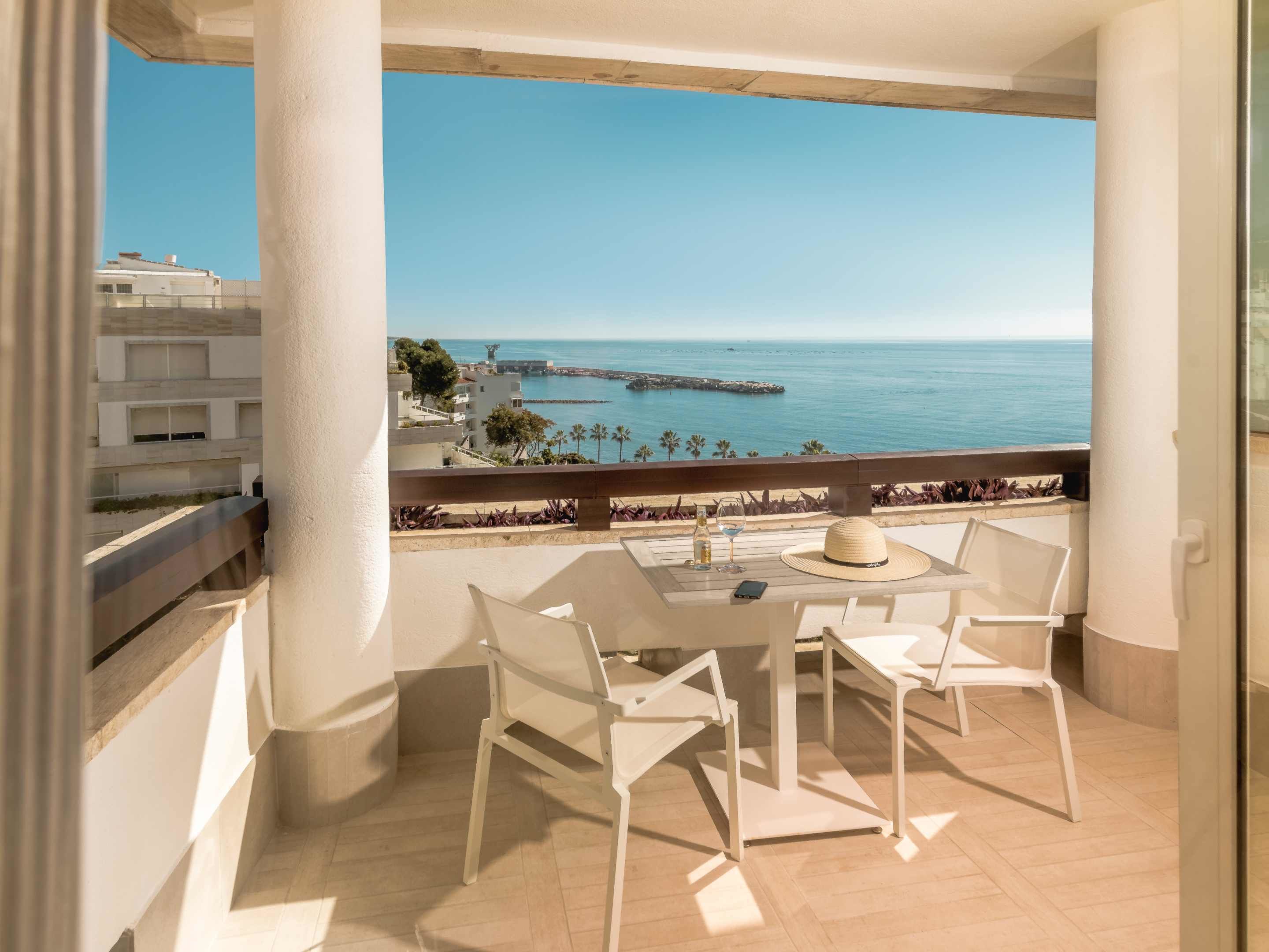 Un balcone con tavolo e sedie, vista sulla costa, edifici e un molo.