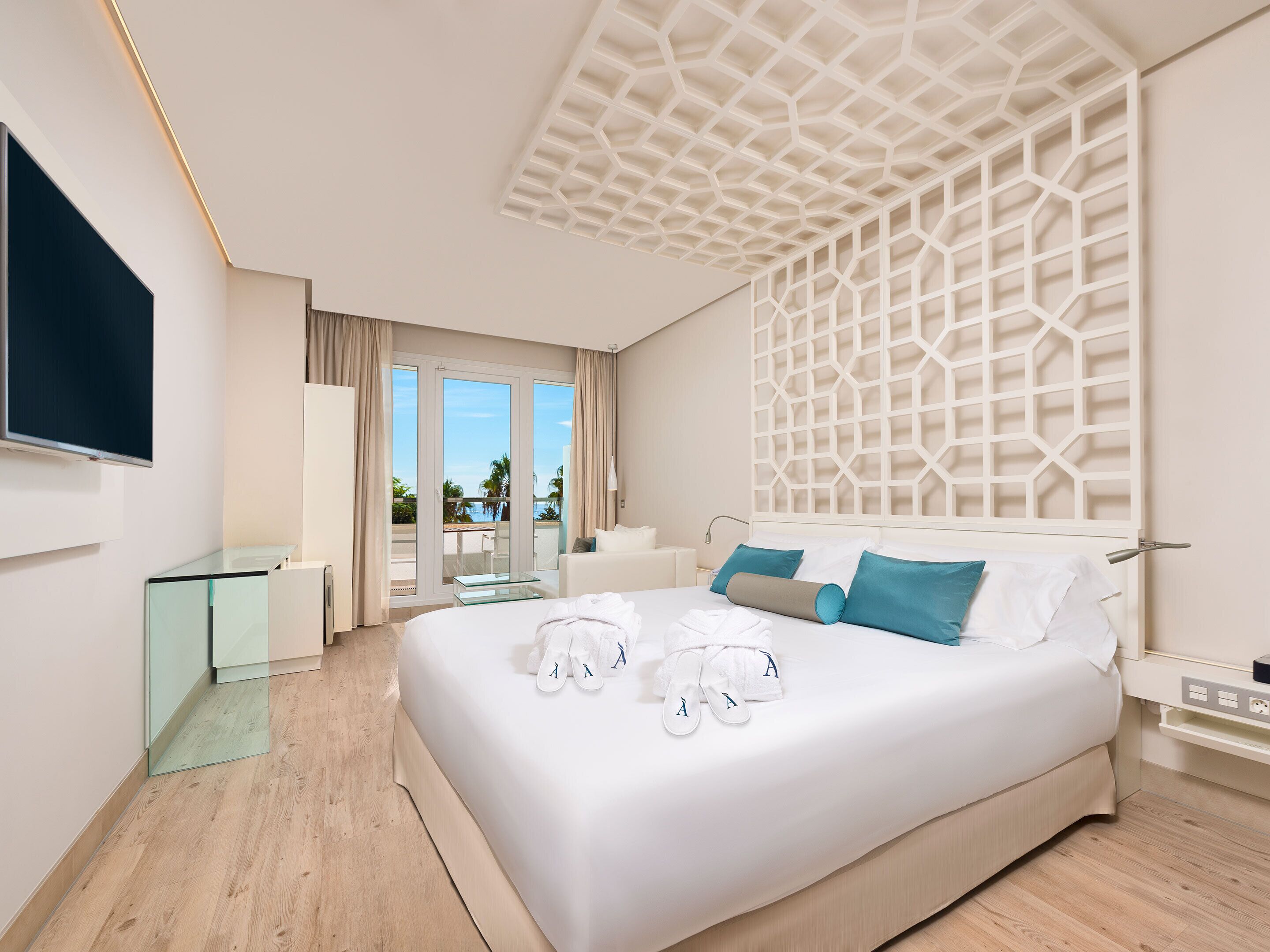 Una habitación de hotel moderna con una cama grande, un televisor de pantalla plana, una mesa de vidrio y un balcón con vistas.