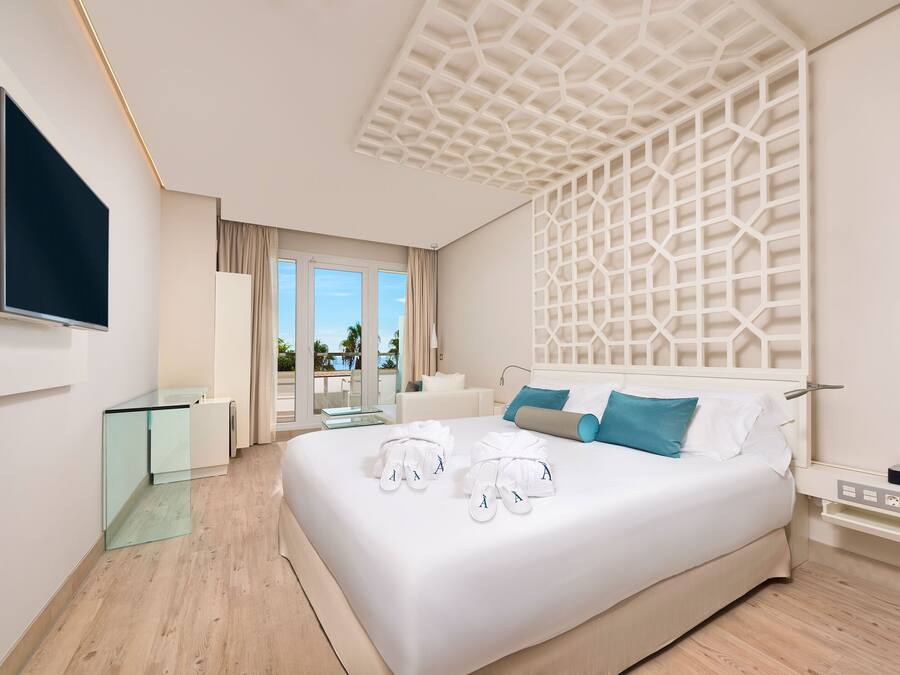 Una habitación de hotel moderna con una cama grande, un televisor de pantalla plana, una mesa de vidrio y un balcón con vistas.