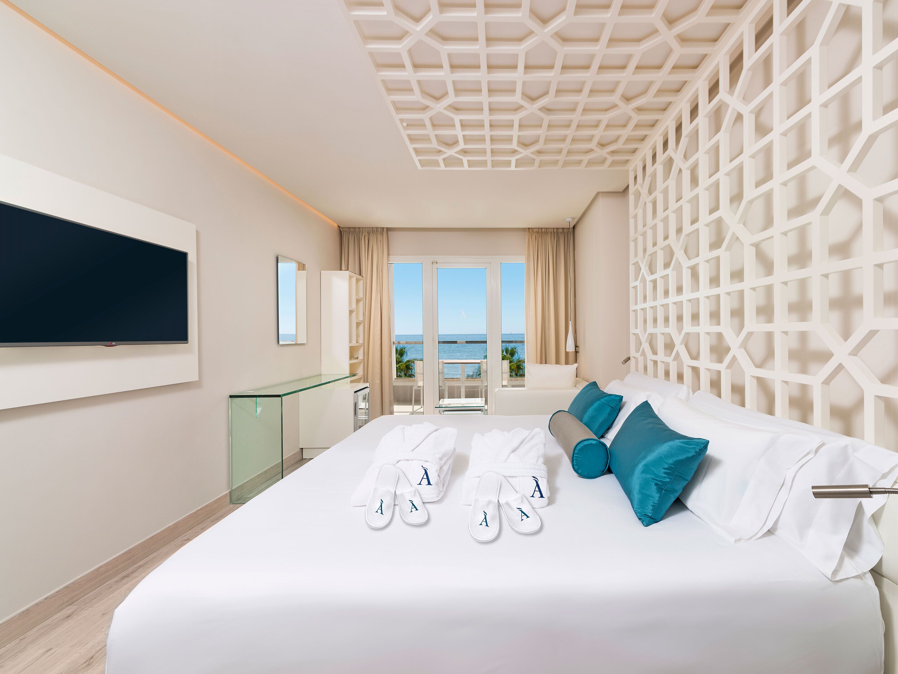 Una habitación de hotel moderna con una cama grande, un televisor montado en la pared y un balcón con vistas al mar.