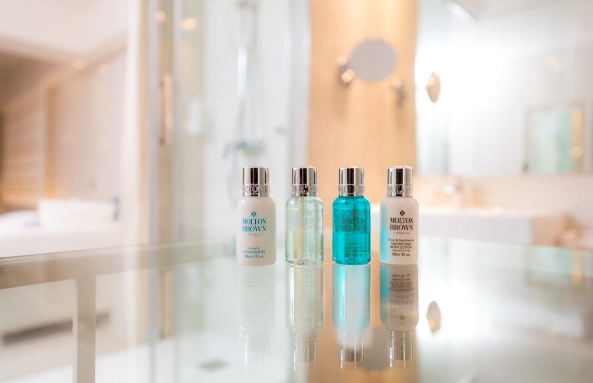 Un baño con una mesa de cristal que muestra tres botellas de acondicionador Molton Brown.