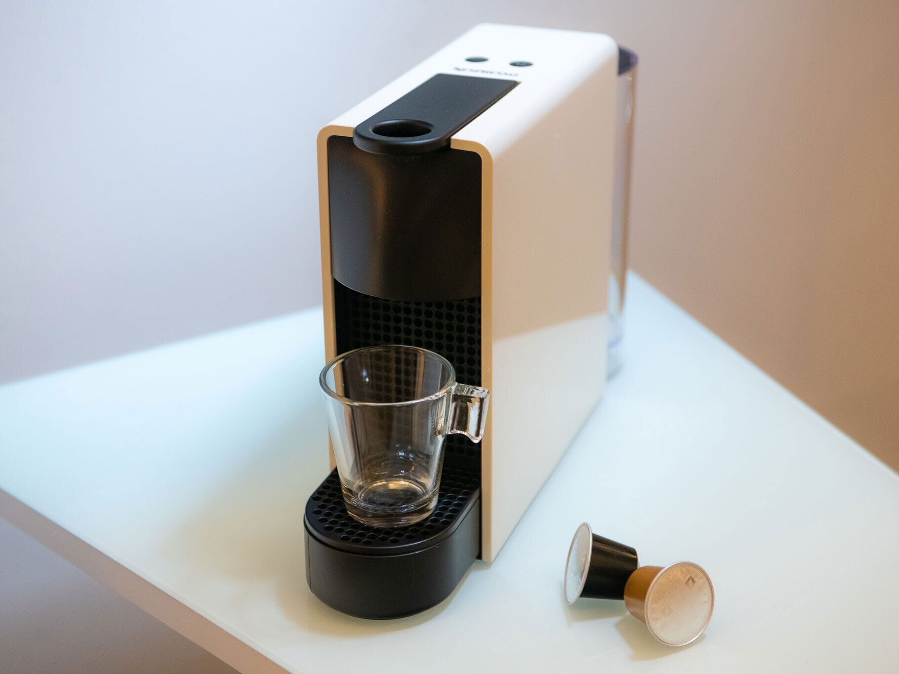 Une machine à café dotée d’un porte-tasse en verre et d’un gobelet jetable, le tout posé sur une surface blanche.