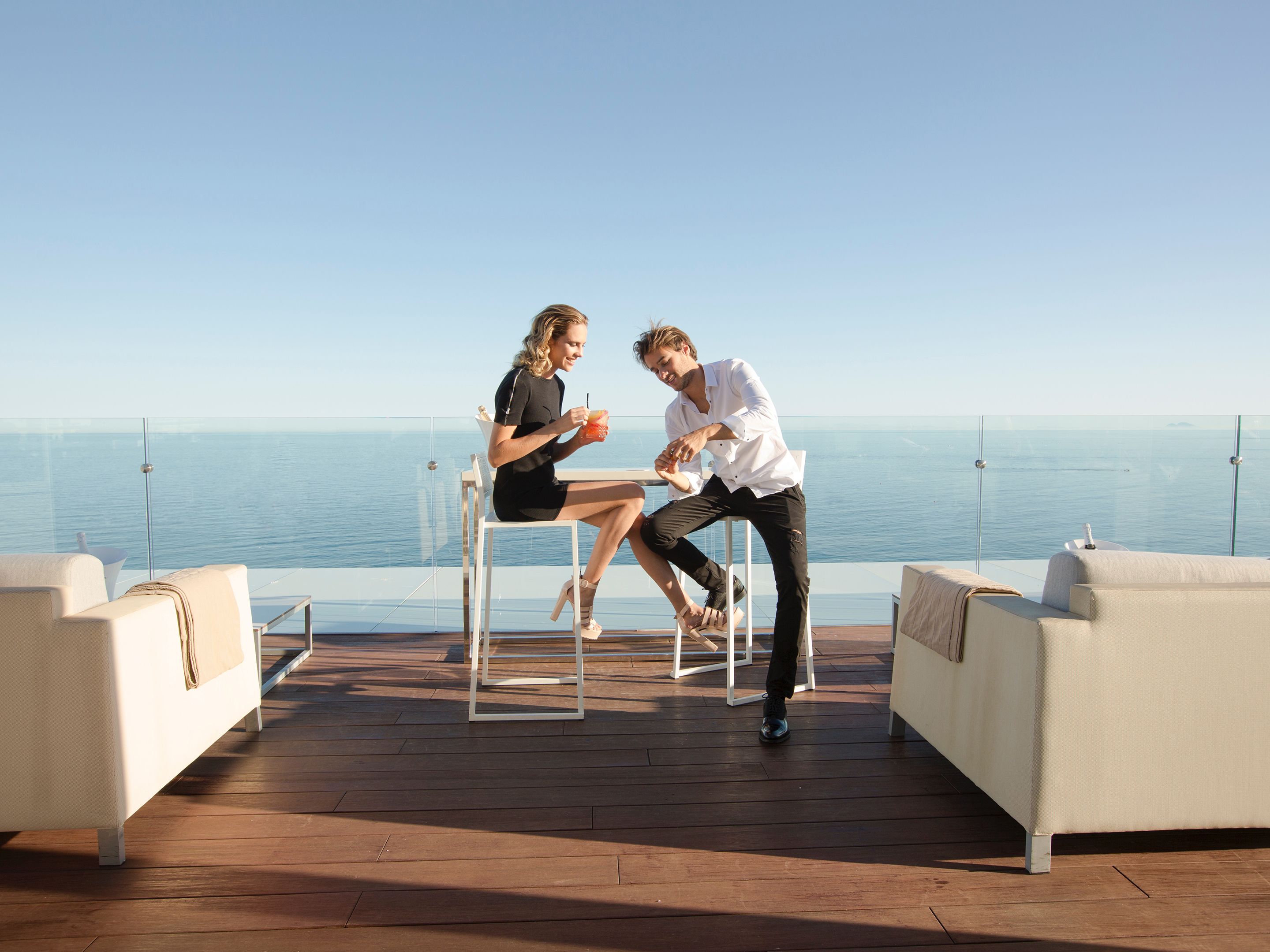 A couple sitting on a deck with a view of the sea.