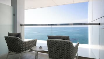 A modern room with a large window overlooking the sea, two chairs with cushions, and a small table.