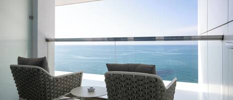 A modern room with a large window overlooking the sea, two chairs with cushions, and a small table.