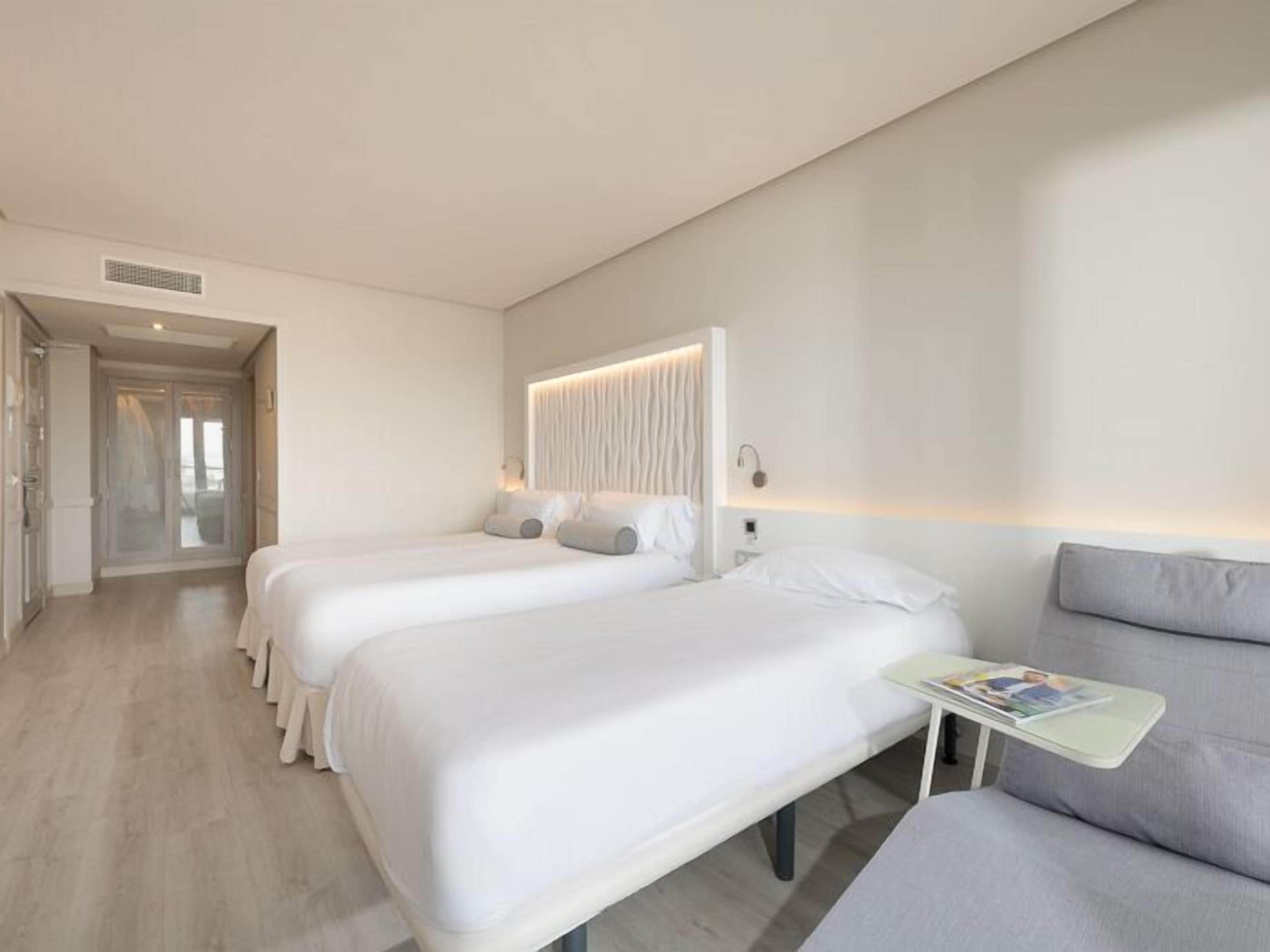 Habitación de hotel con dos camas, un sofá y una pequeña mesa con revistas.
