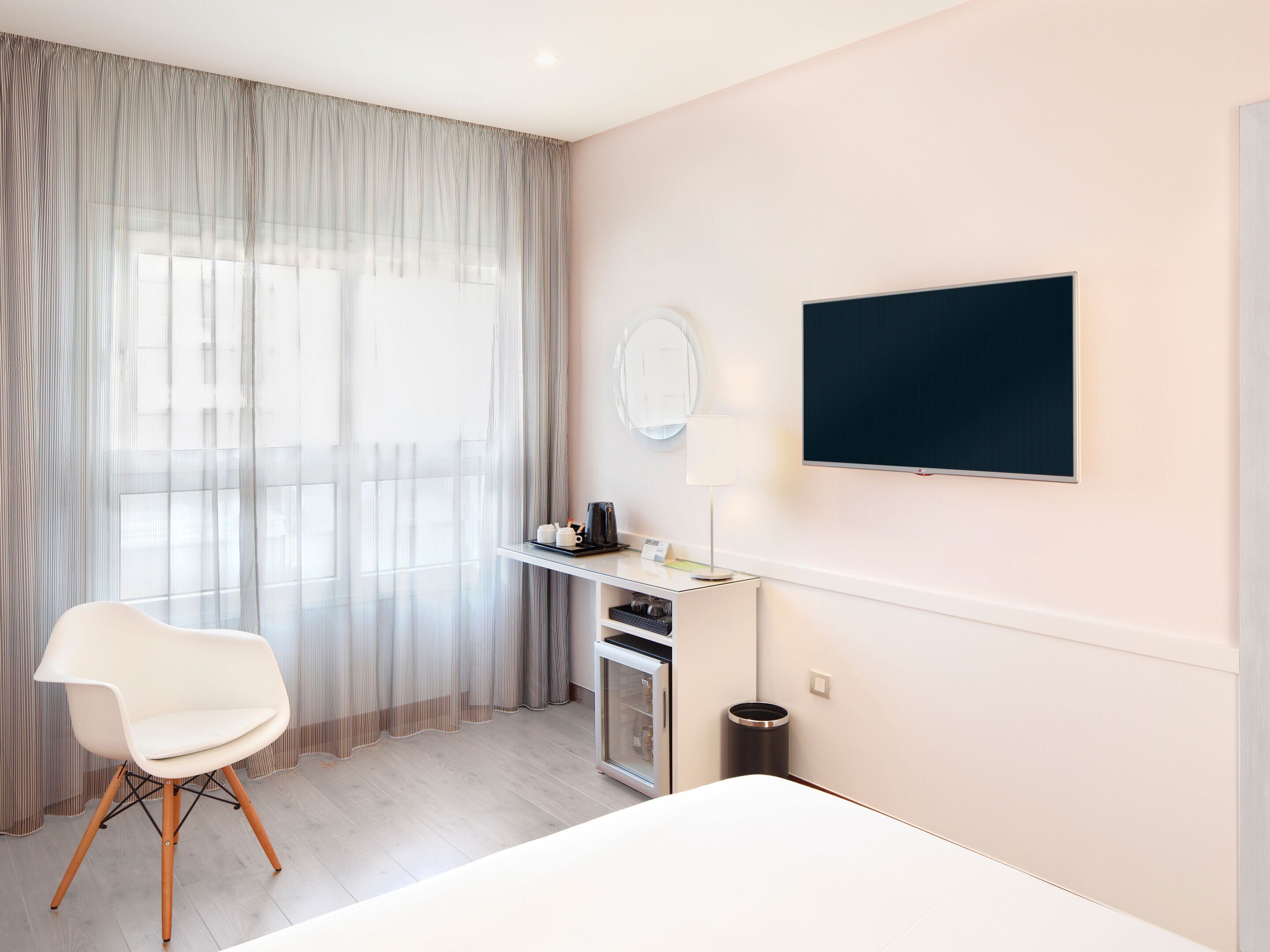 Camera d'albergo con un letto, una scrivania con un computer, una sedia, una televisione e una finestra con tende.