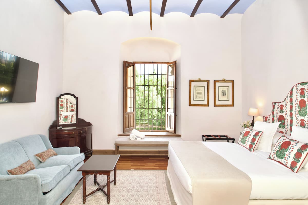 Un dormitorio con cama, sofá, ventana con rejas, televisor y cuadros en la pared.