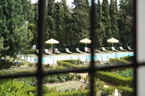 A pool area with lounge chairs and umbrellas, surrounded by greenery and trees. - Monasterio de San Francisco (Palma del Rio)