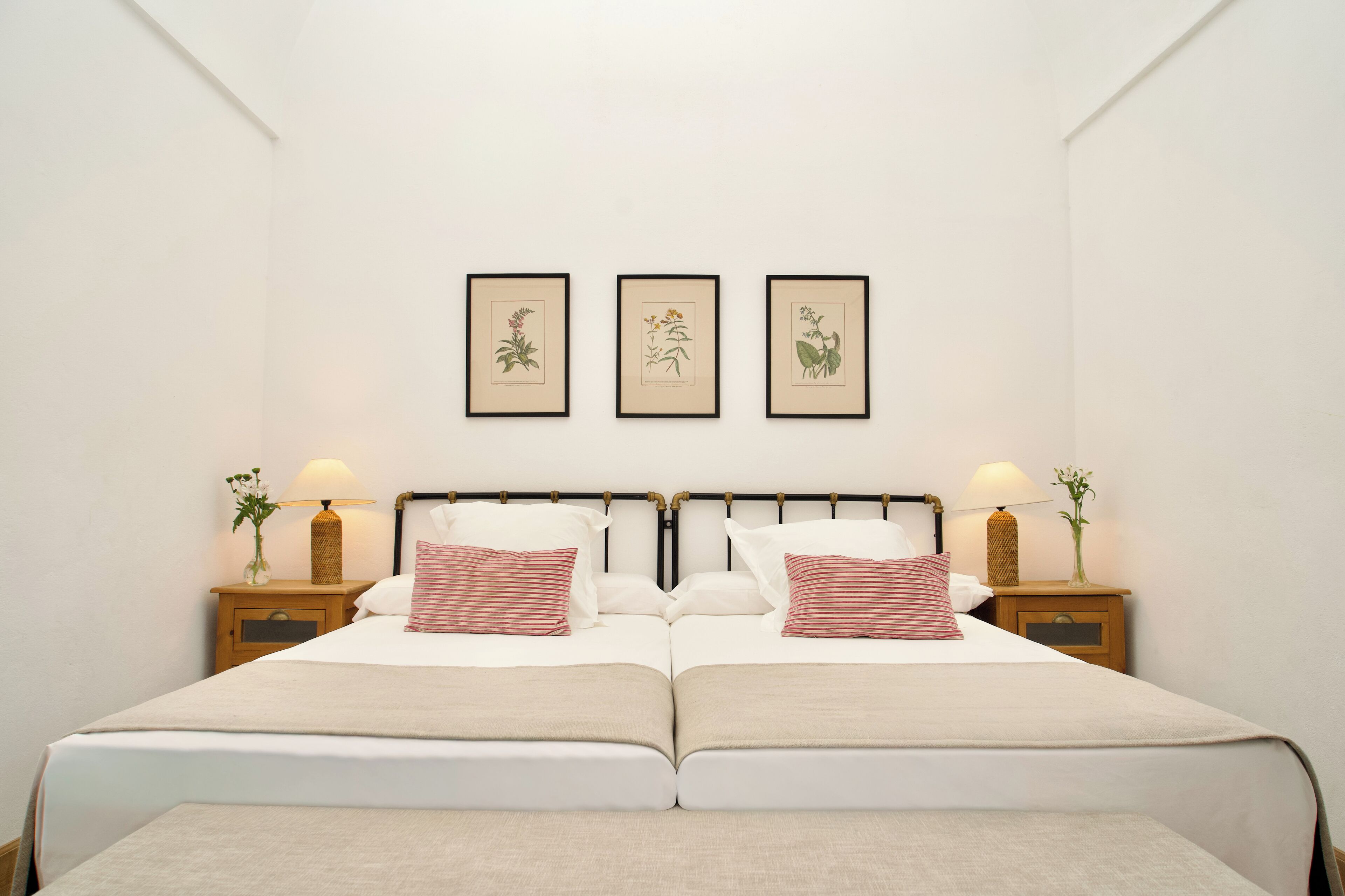 Un letto matrimoniale con due comodini, ognuno dotato di lampada e vaso. Sopra il letto, tre stampe botaniche in cornice.
