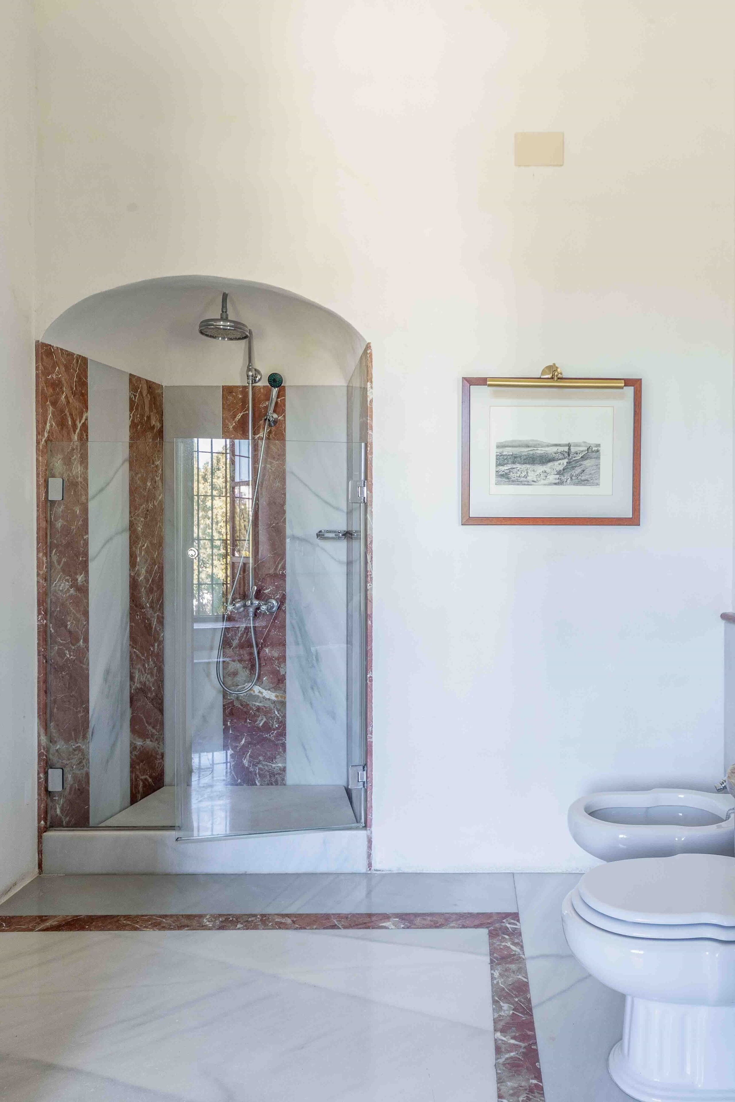 A bathroom with a glass-enclosed shower, a toilet, and a framed picture on the wall.
