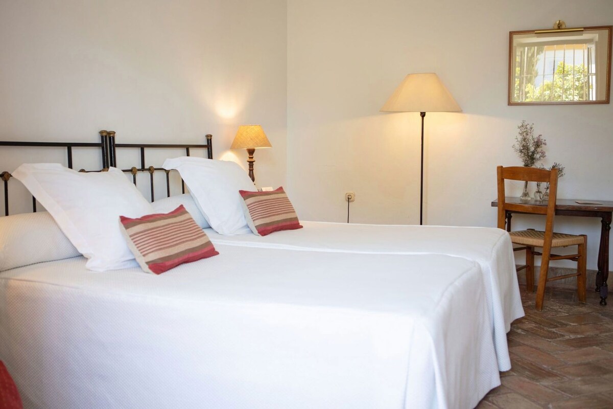 Quarto de hotel com duas camas, uma mesa e uma cadeira.
