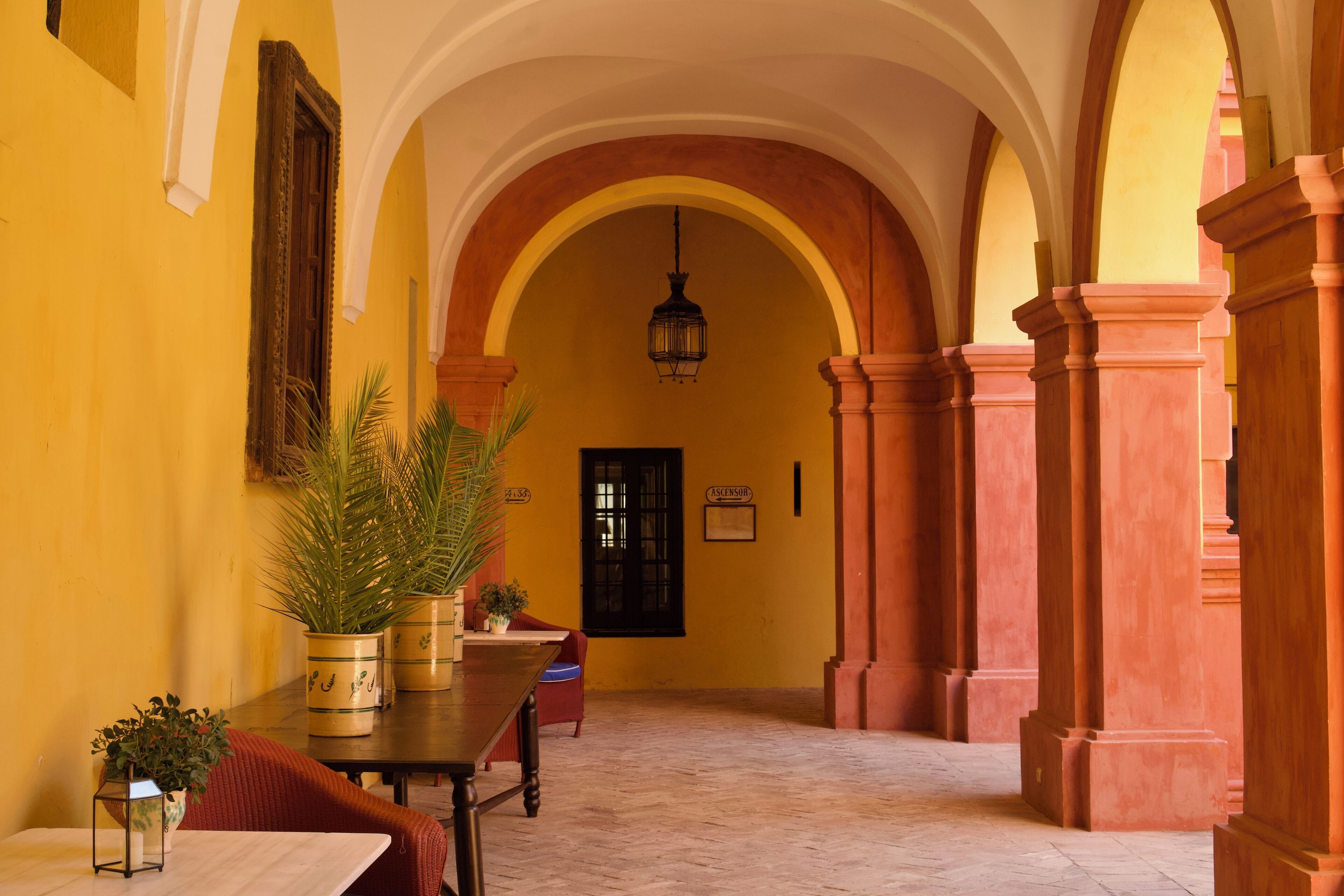 Un pasillo interior con arcos, una mesa con plantas en macetas y una puerta con la etiqueta 'ASESSOR'.