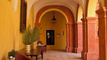 Un pasillo interior con arcos, una mesa con plantas en macetas y una puerta con la etiqueta 'ASESSOR'.