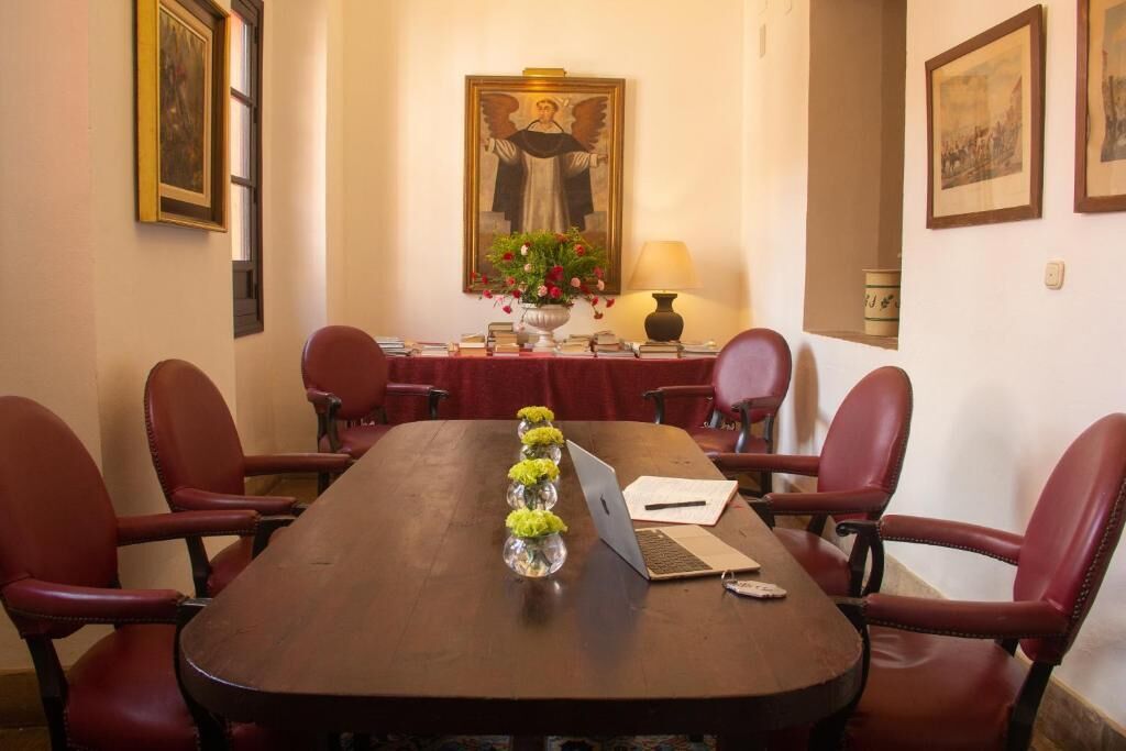 A conference room with a long table, red chairs, a laptop, and a vase with flowers.