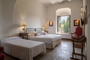 Two single beds with white bedspreads and pillows, a nightstand with a lamp, and a small table with a vase of flowers.