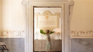 Una escalera de mármol que conduce a una puerta con una placa, una planta en maceta y un candelabro.