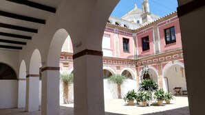 Un patio con arcos, plantas en macetas y un edificio con tejado de baldosas al fondo.