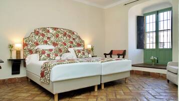Una cama doble con cabecera floral, dos lámparas de noche y una puerta verde al fondo.