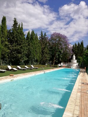A swimming pool with lounge chairs and a white structure in the background. - Monasterio de San Francisco (Palma del Rio)