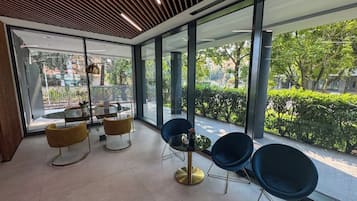 Un ambiente interno moderno con parete in vetro, soffitto in legno e una zona relax con tavoli e sedie rotonde.