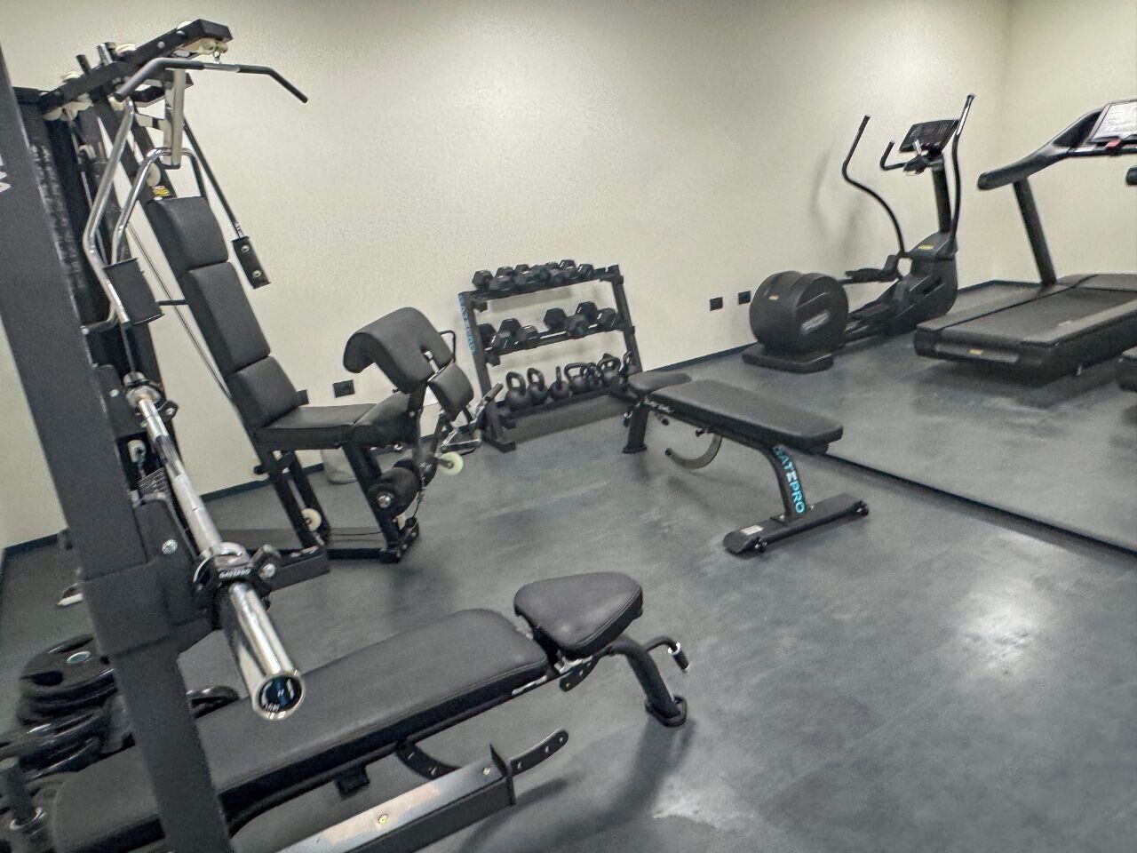 Une salle de sport équipée de matériel de musculation, notamment un banc, des haltères et un tapis de course.