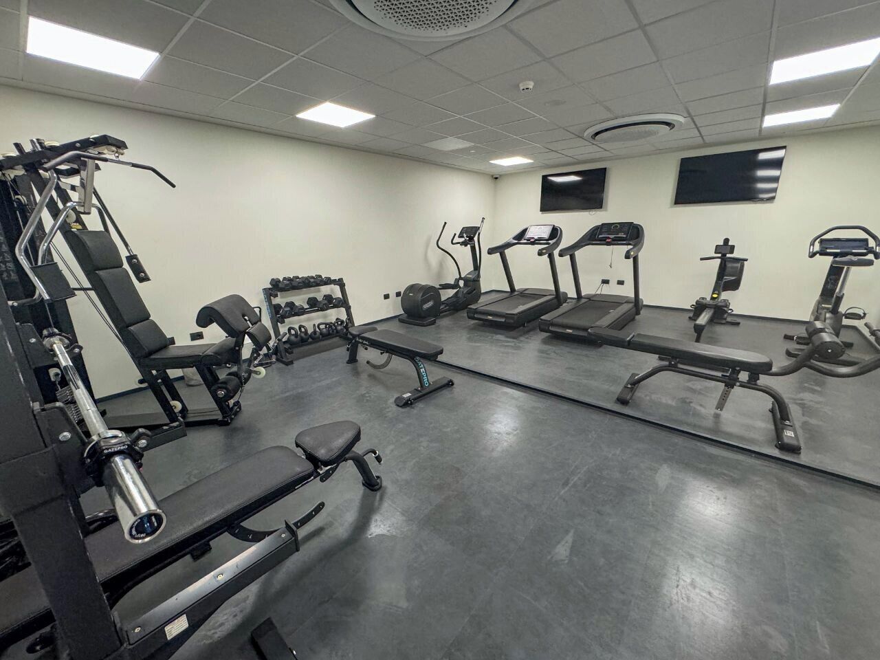 Ein Fitnessraum mit unterschiedlichen Trainingsgeräten, darunter Laufbänder, Kraftgeräte und Kurzhanteln.