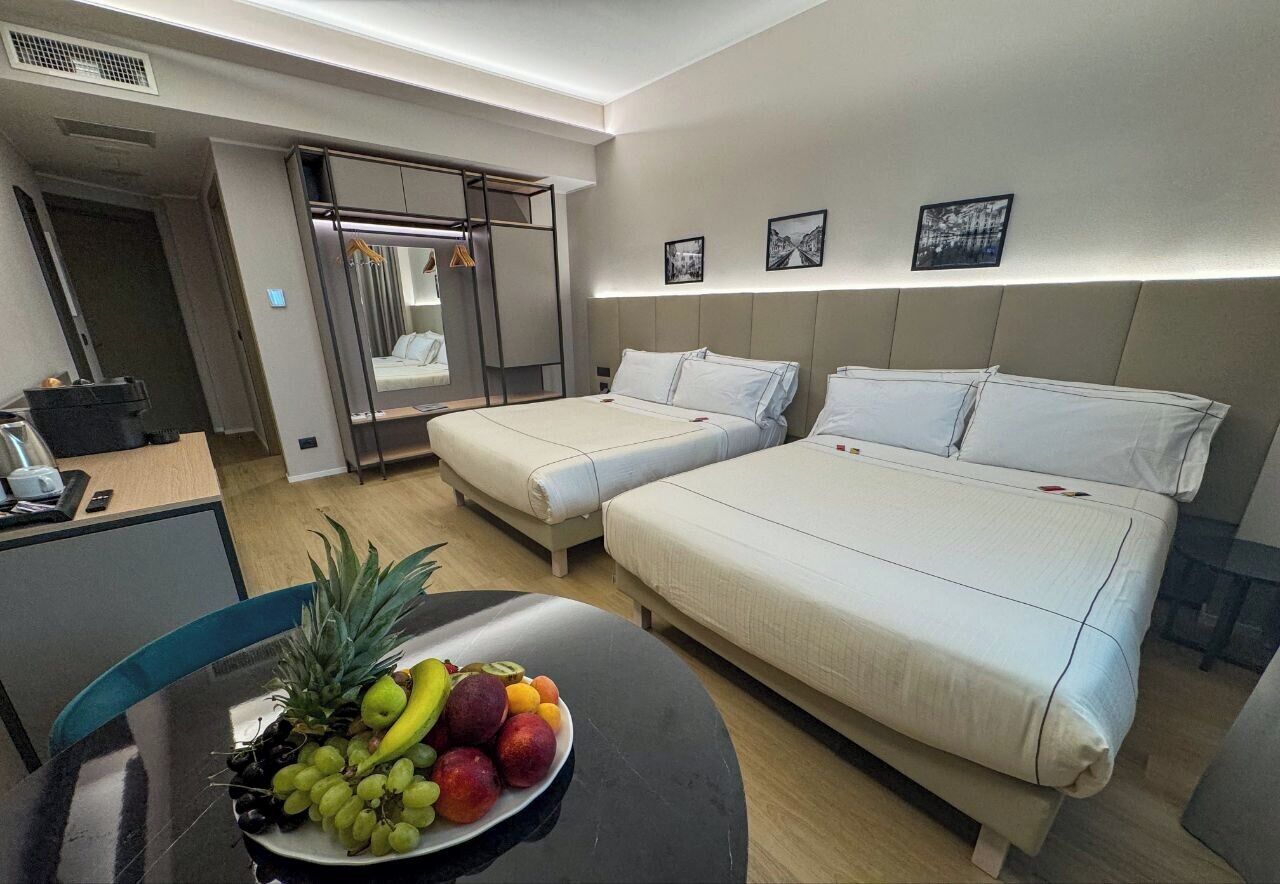 Een hotelkamer met twee bedden, een eettafel met fruit en een kledingkast.