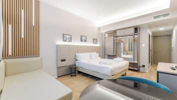 Ein modernes Hotelzimmer mit Bett, Nachttisch, Sessel und Schreibtisch mit Stuhl.