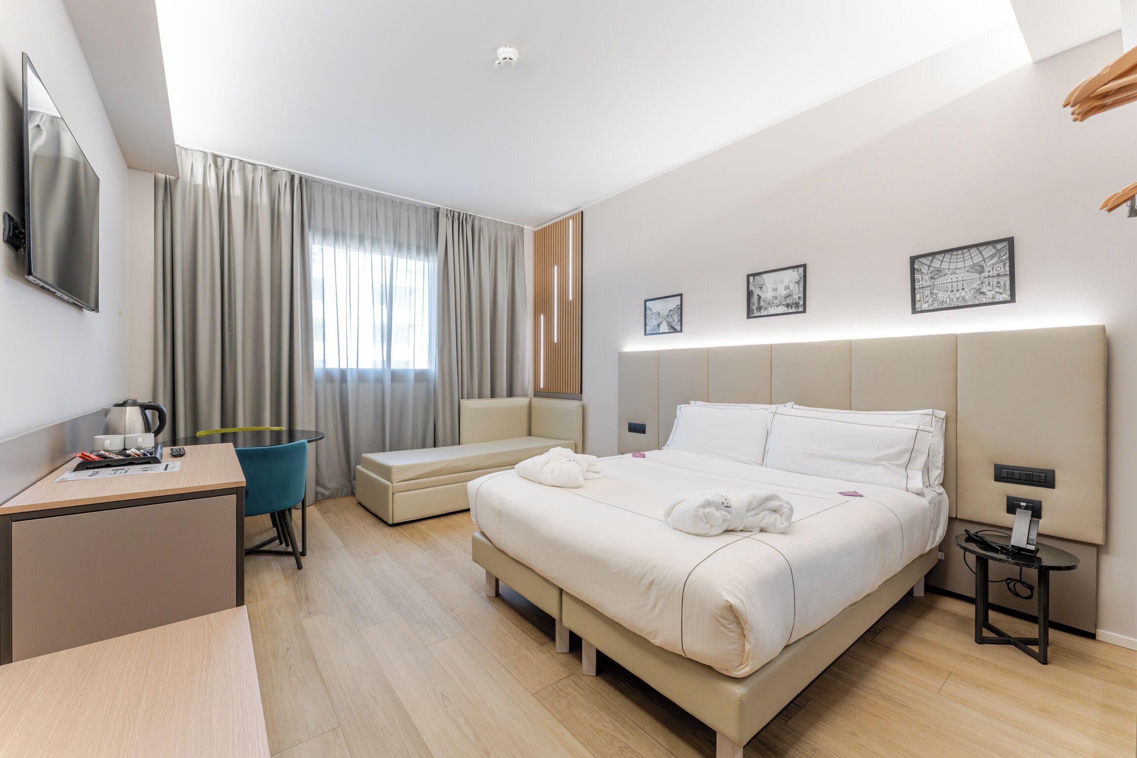 Une chambre d’hôtel moderne équipée d’un lit, d’un bureau, d’une chaise et d’un téléviseur fixé au mur.