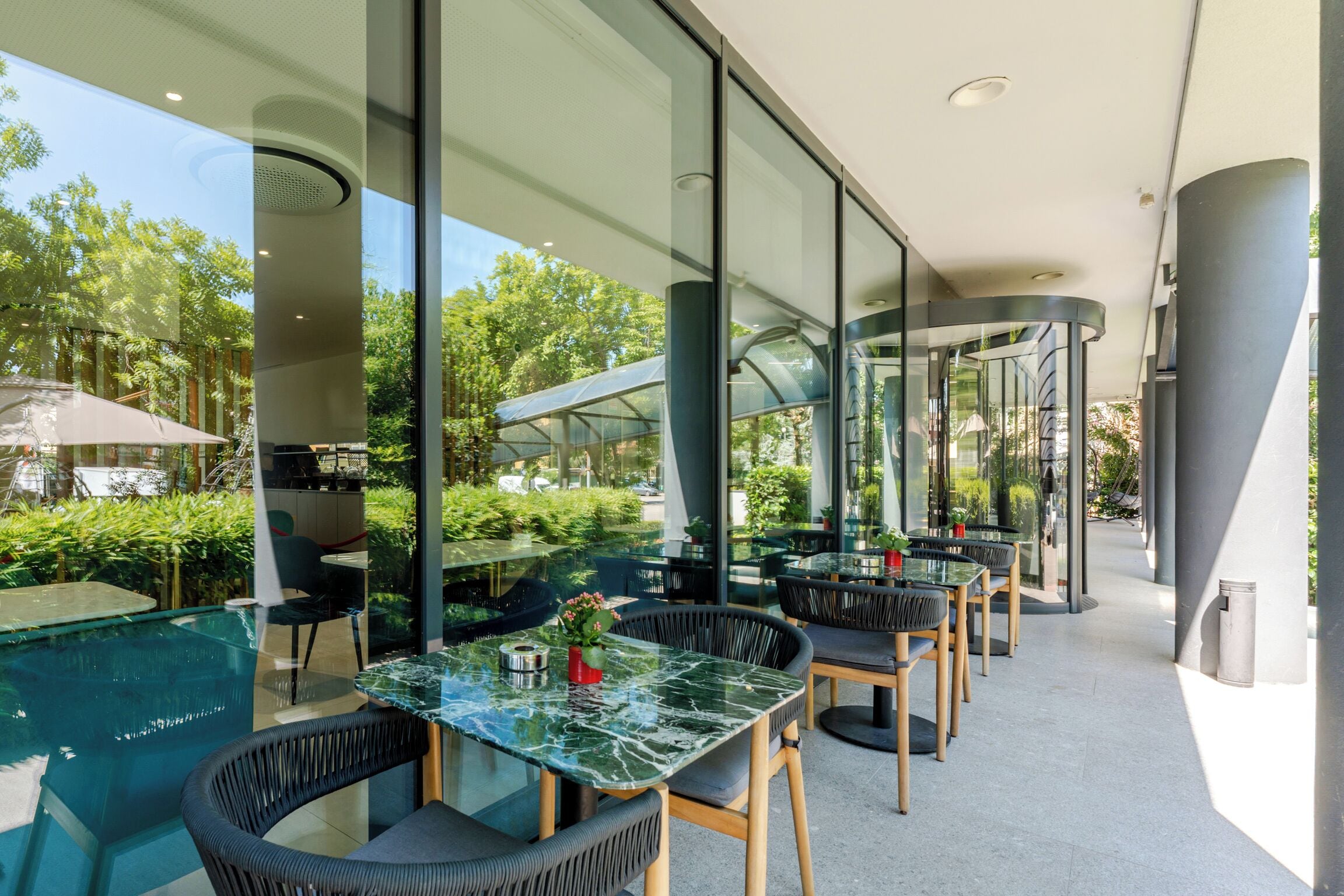 An outdoor dining area with glass walls, tables, chairs, and a pool.