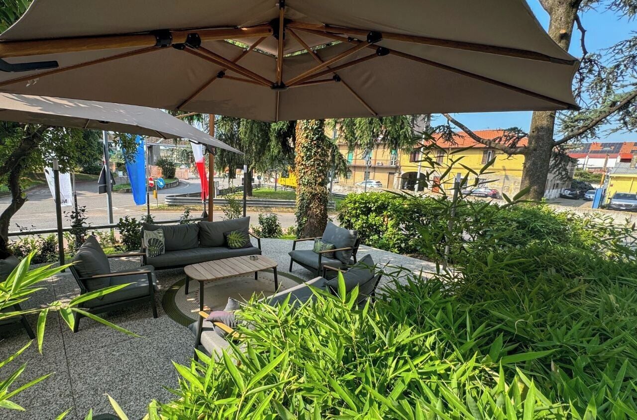 Un espace extérieur aménagé avec une table et des chaises, entouré de verdure et abrité par un grand parasol.