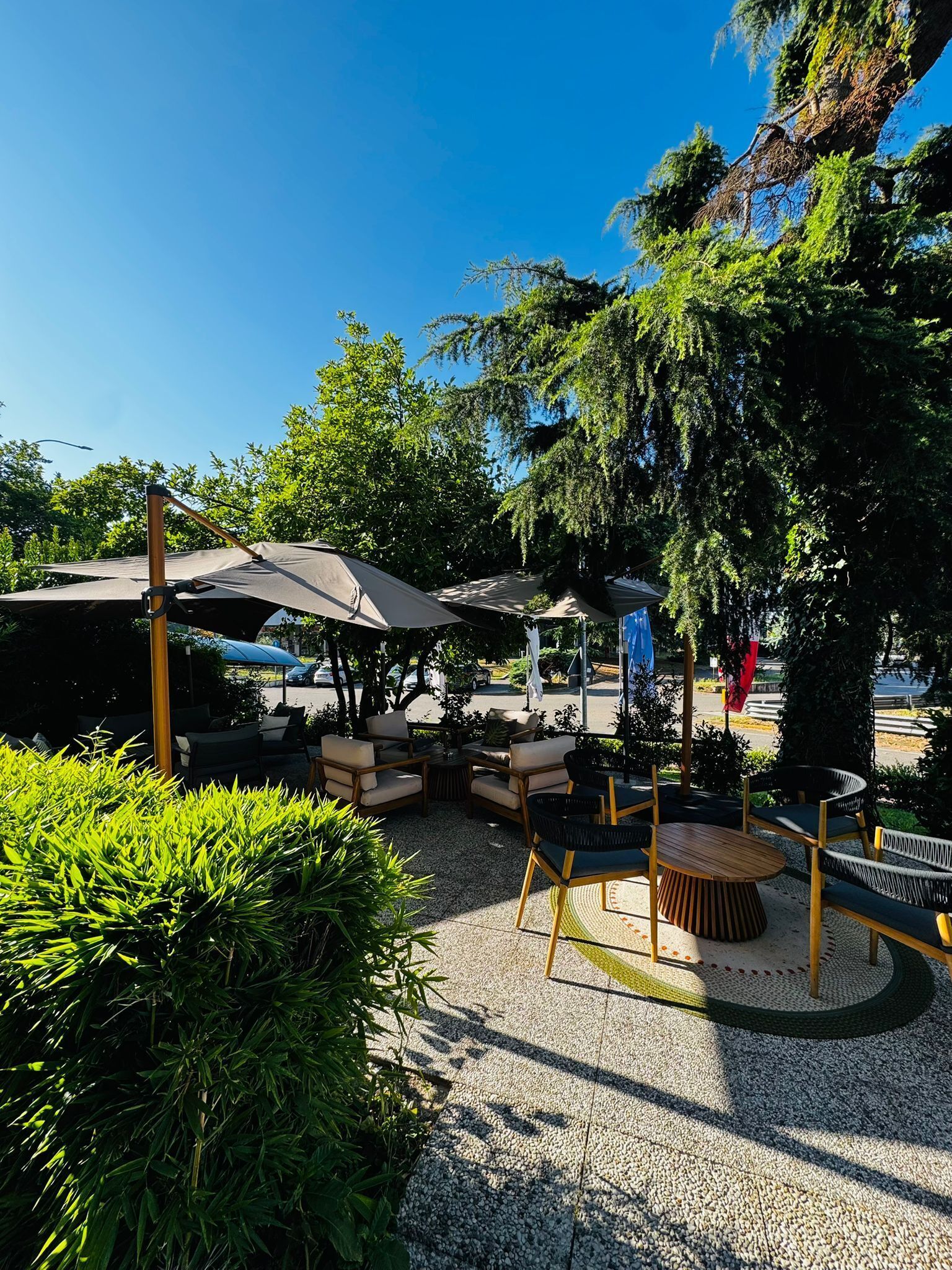 An outdoor seating area with tables and chairs, surrounded by greenery and umbrellas.
